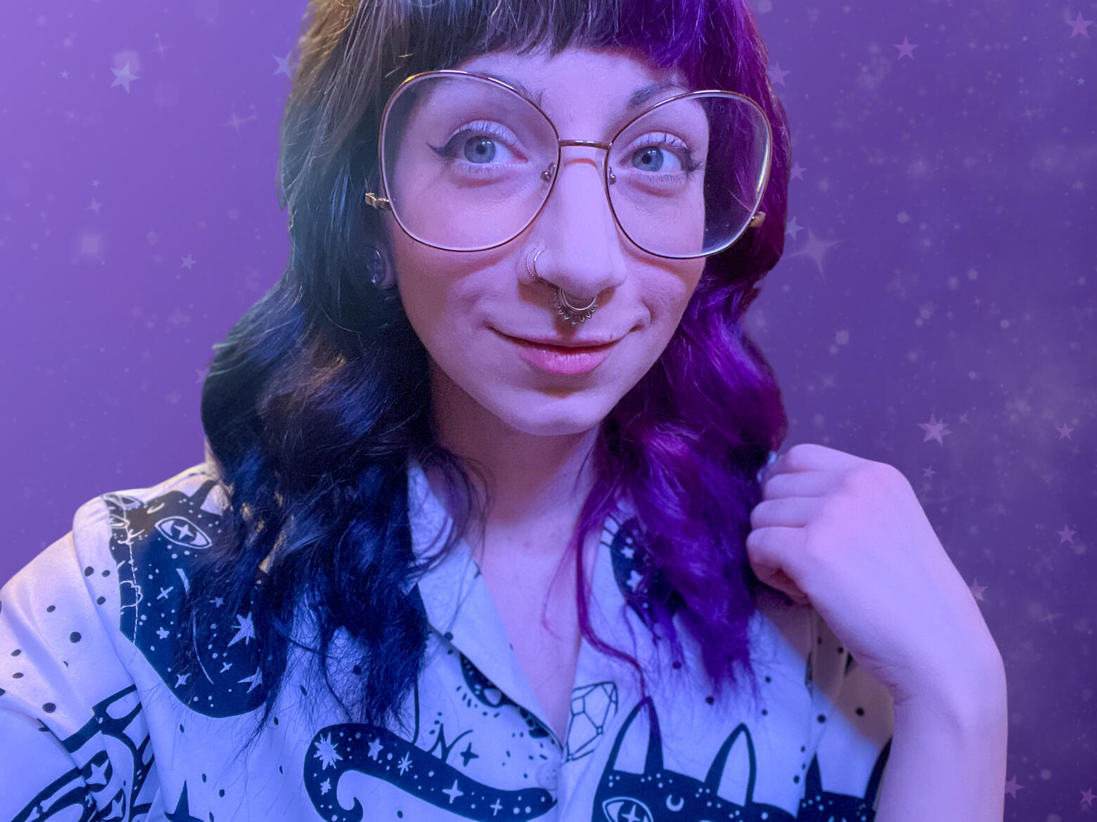 Photo of Zoe with purple & black split hair. She is wearing wired glasses as well as a white top. She is slightly smiling & looking to the left of the camera.